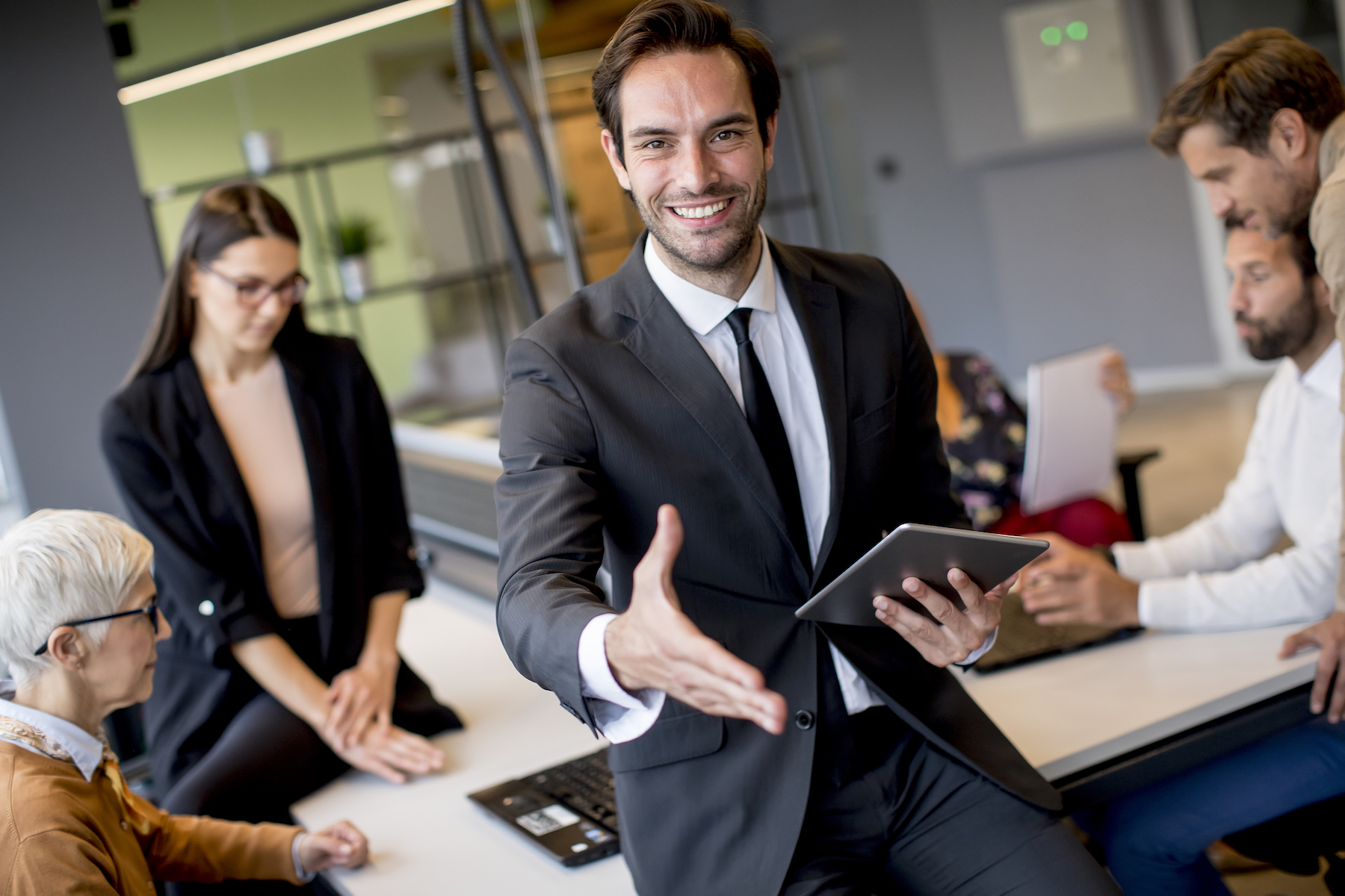 Young businessman using digital tablet in office in front of his team