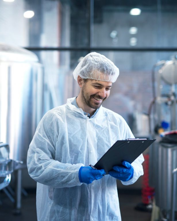 industrial-worker-technologist-in-white-suit-with-hairnet-and-protective-gloves-looking-at-checklist-and-smiling